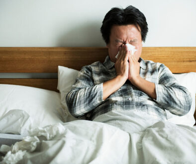 An Asian Man Sitting in Bed Blowing His Nose Hay Fever vs Cold Symptoms