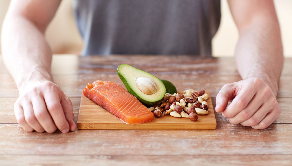 Closeup Of Fish, Avocado, & Nuts On A Cutting Board In Front Of A Man Foods To Prevent Colon Cancer