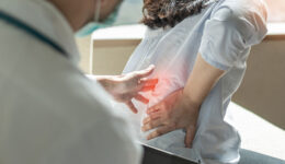 A Primary Care Doctor Pressing On A Patient’s Spine As She Grabs Her Back In Pain Stages Of Osteoporosis