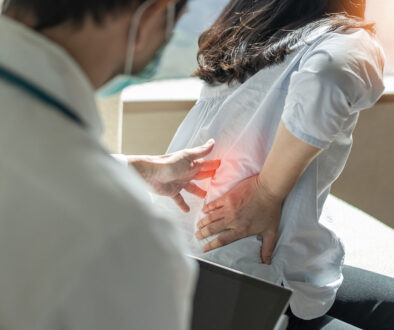 A Primary Care Doctor Pressing On A Patient’s Spine As She Grabs Her Back In Pain Stages Of Osteoporosis